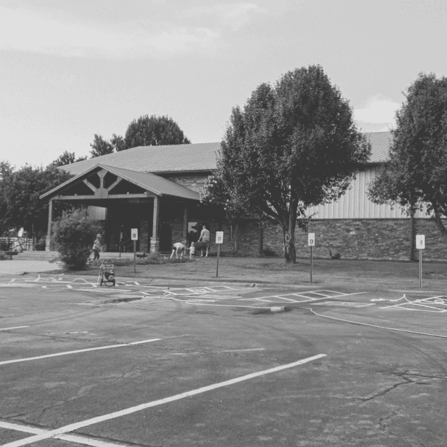 Community church building with parking lot and trees, outdoor setting.